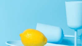 A lemon on a plate with two cups and a glass.